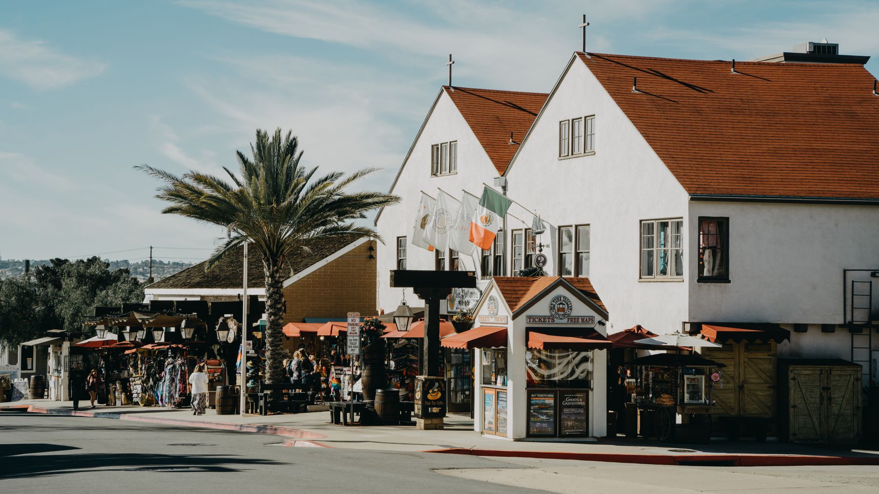 A sunny commercial street in San Diego's Old Town with pedestrians, storefronts, and palm trees